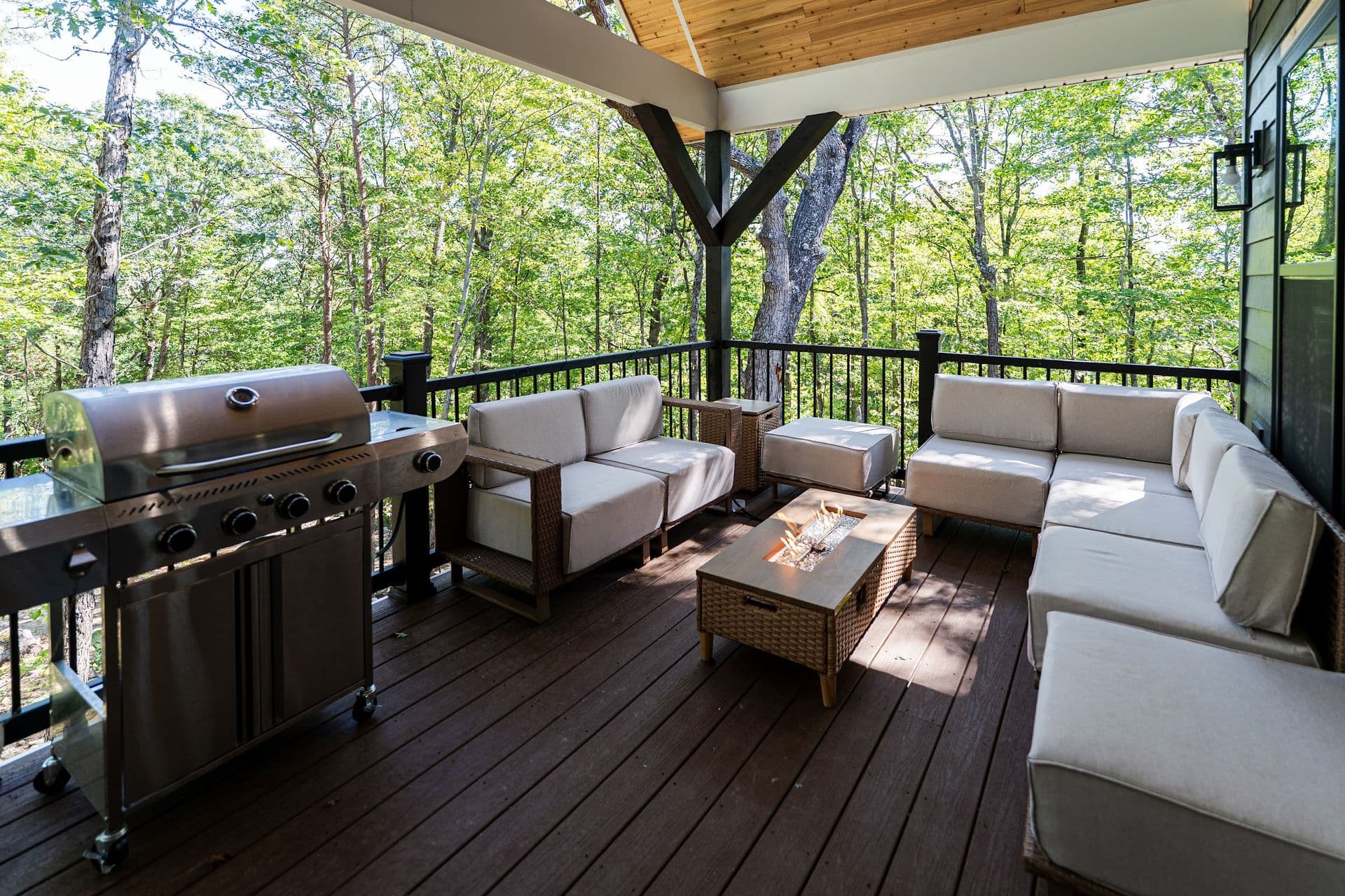 The 25 x 10 ft covered back deck: grill, sectional sofa and fire table looking into the trees