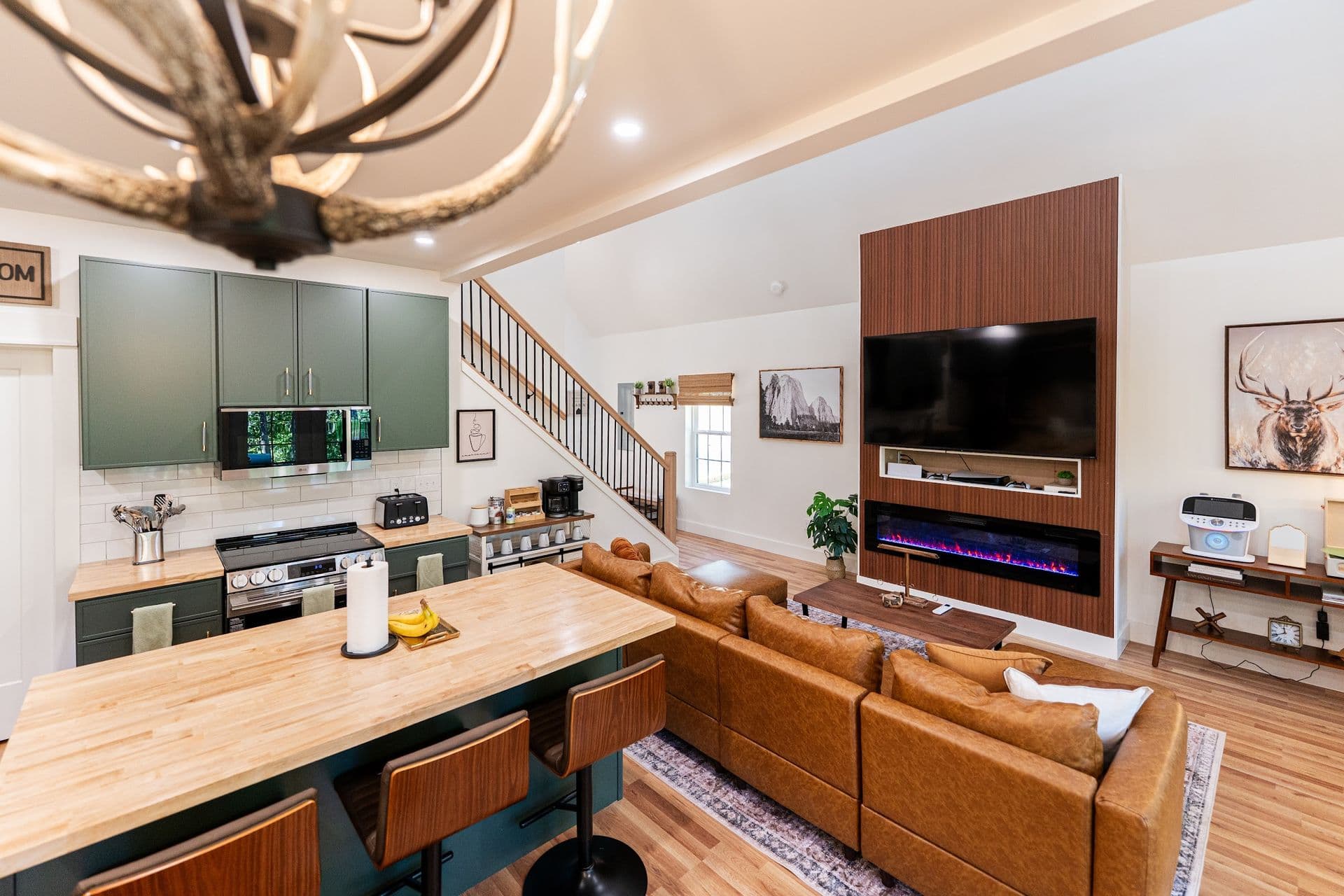 The Stag's great room seen from the loft, with the kitchen island, leather sectional and fireplace wall under an antler chandelier