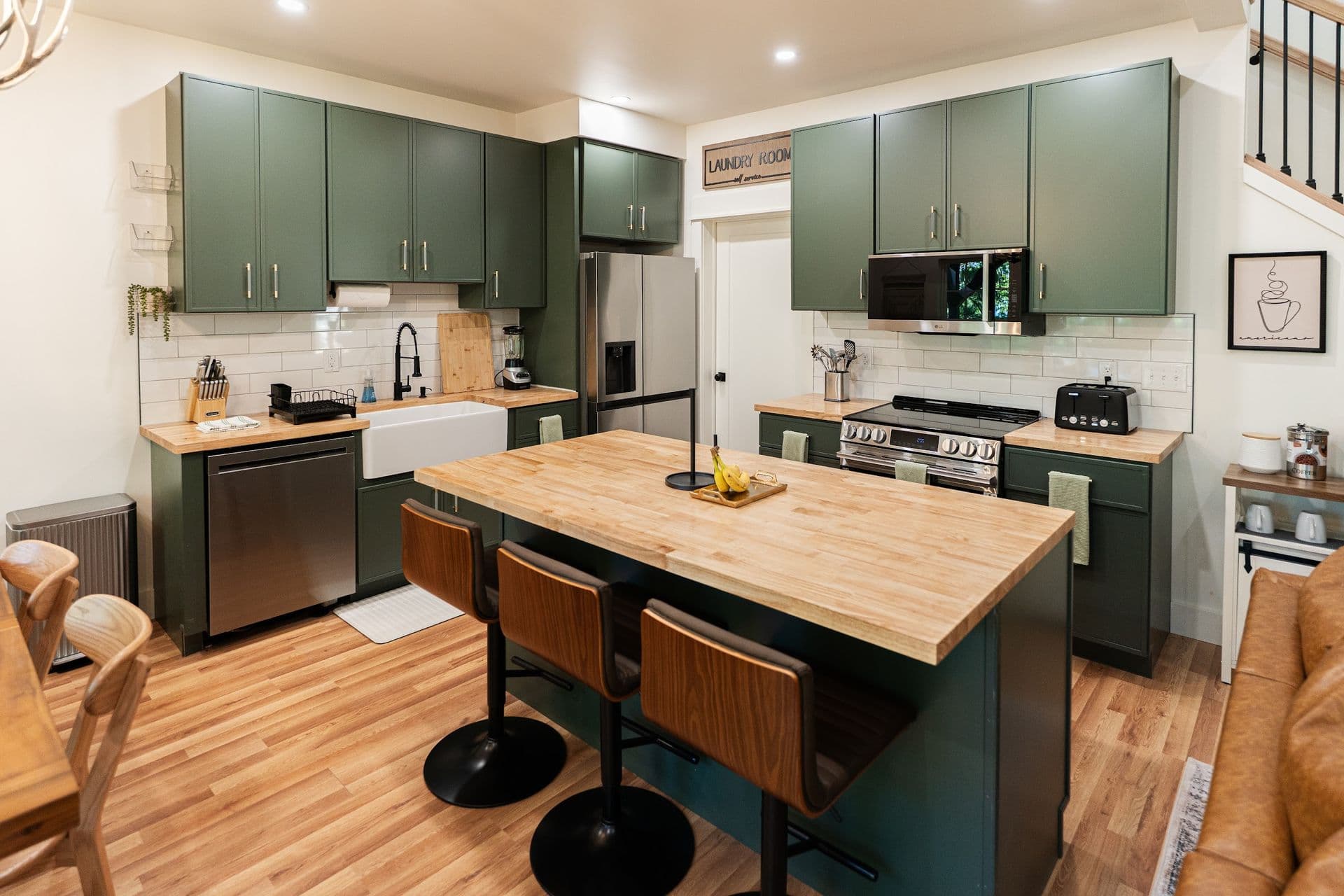 The green kitchen with its butcher-block island and three bar stools