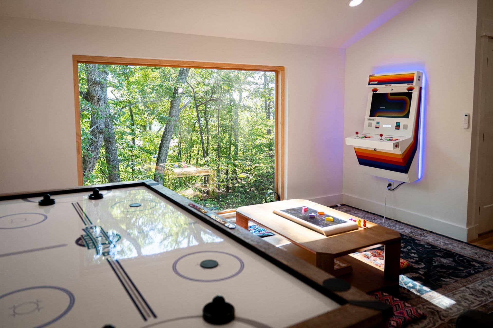 The game loft: air hockey in front of the 6 x 7 ft picture window, with the Polycade arcade lit on the wall