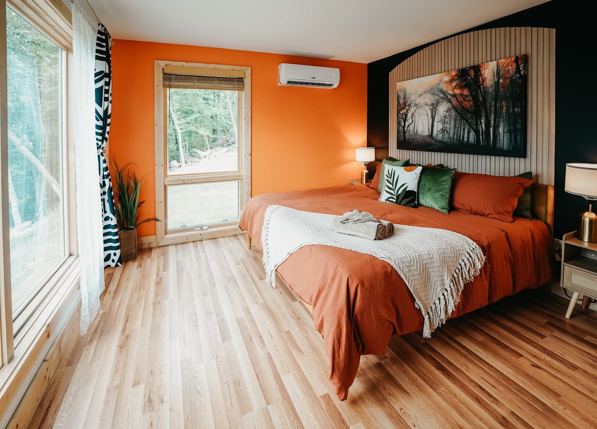 The king bed against the orange accent wall, with windows to the trees