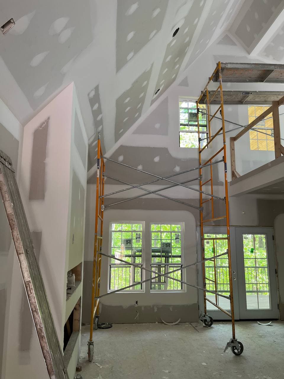 Drywall complete — vaulted great room with tall windows